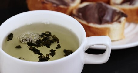 Wall Mural - Green tea brewed in a mug and a baguette with chocolate butter, a delicious sweet dessert with chocolate cream and green hot tea