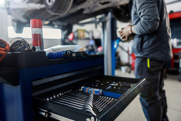 Wall Mural - Selective focus on wrenches and tools at the mechanic's workshop with worker repairing the car in blurry background.