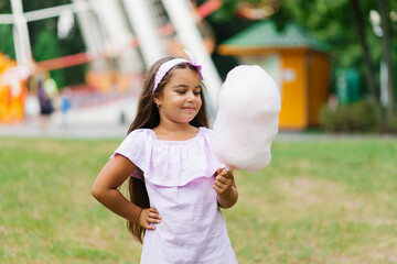 Wall Mural - A cute dark-skinned girl in a pink dress holds cotton candy in her hands in the summer in the park