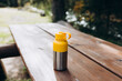 A yellow vacuum theroms stands on a tree desk in the wild. Hiking equipment on footpath in woodland. Travel outdoor concept