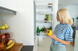 © Westend61 - Smiling woman with yellow bell pepper using smart phone near fridge at home