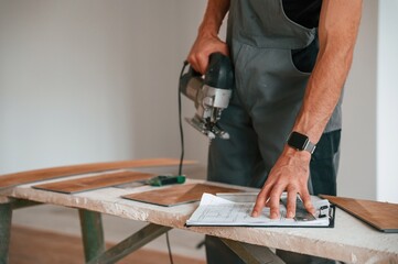 Wall Mural - Standing by the table with jigsaw. Man is installing new laminated wooden floor