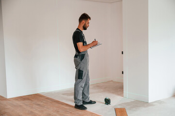 Wall Mural - Making notes into the document and using laser leveler. Man is installing new laminated wooden floor