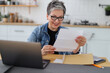 © Andrii Zastrozhnov - Happy mature woman watching mail bank notice, sitting at kitchen table at home.