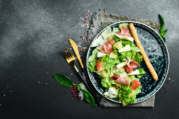 Wall Mural - Fresh salad: prosciutto, brie cheese and pineapple. On a dark background, close-up.