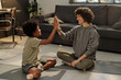 © pressmaster - Happy young woman in activewear and her adorable son giving each other high five after workout while sitting on the floor of living room