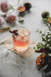 Refreshing healthy natural fruit cocktail in a glass with passion fruit, basil and ice on a table with flowers and fruits.