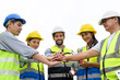 © bigy9950 - Group of contractors, engineers and formats in safety vests with helmets join hands to work together to successfully complete a construction project on construction site. success concept.