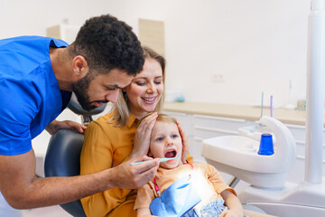 Wall Mural - little girl sitting with her mother on dentist chair, during preventive examination.