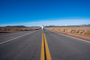 older man standing in the middle of a desert road with arms outstretched. high quality photo