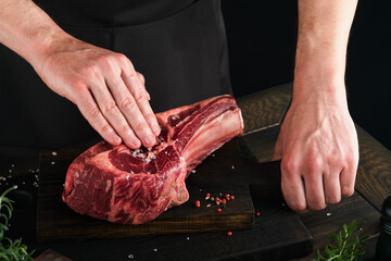 Chef cutting steak beef. Mans hands hold raw steak Tomahawk on rustic wooden cutting board on black background. Cooking, recipes and eating concept. Selective focus.