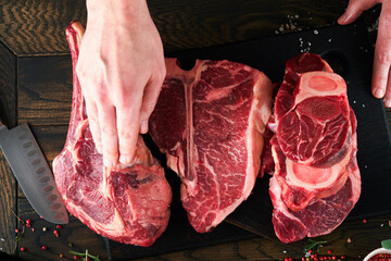 Chef cutting steak beef. Mans hands hold raw steak Tomahawk on rustic wooden cutting board on black background. Cooking, recipes and eating concept. Selective focus.