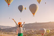 © EdNurg - Happy traveller girl raising hands while watching magnificent view of flying hot air balloons in famous tourist attraction - Cappadocia