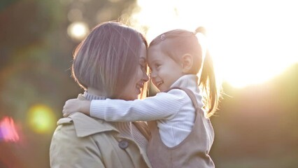 an adorable, sweet little girl hugs her young mother during a walk in a spring park.
