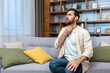 © Liubomir - Sore throat. A young man sits at home on the sofa and holds his throat, feels a sore throat, burning sensation, discomfort.