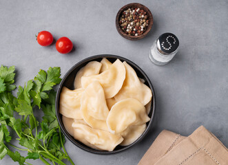 Wall Mural - Dumplings with vegetables. Delicious vegetarian vareniki  in a bowl  on a gray background with herbs.