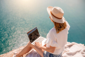 Freelance women sea working on the computer. Good looking middle aged woman typing on a laptop keyboard outdoors with a beautiful sea view. The concept of remote work.