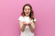© Богдан Маліцький - young cute woman in white t-shirt holds empty hands in front of her on pink isolated background