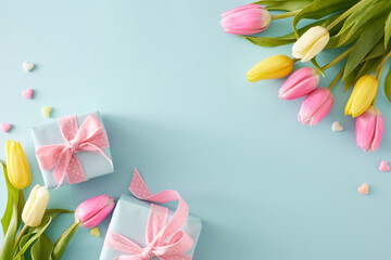 Wall Mural - Mother's Day concept. Top view composition of gift boxes with bows colorful hearts and bouquets of flowers yellow pink tulips on pastel blue background with empty space in the middle