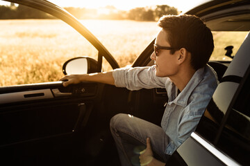 Young attractive man sitting in his car smiling feeling happy enjoying the nature view. 