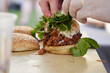 Chef places fresh herb ingredients on top of delicious pulled pork sandwich at farmers market for customer
