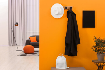 Sticker - Hat, coat, backpack and houseplant near orange wall in stylish room, space for text. Interior design