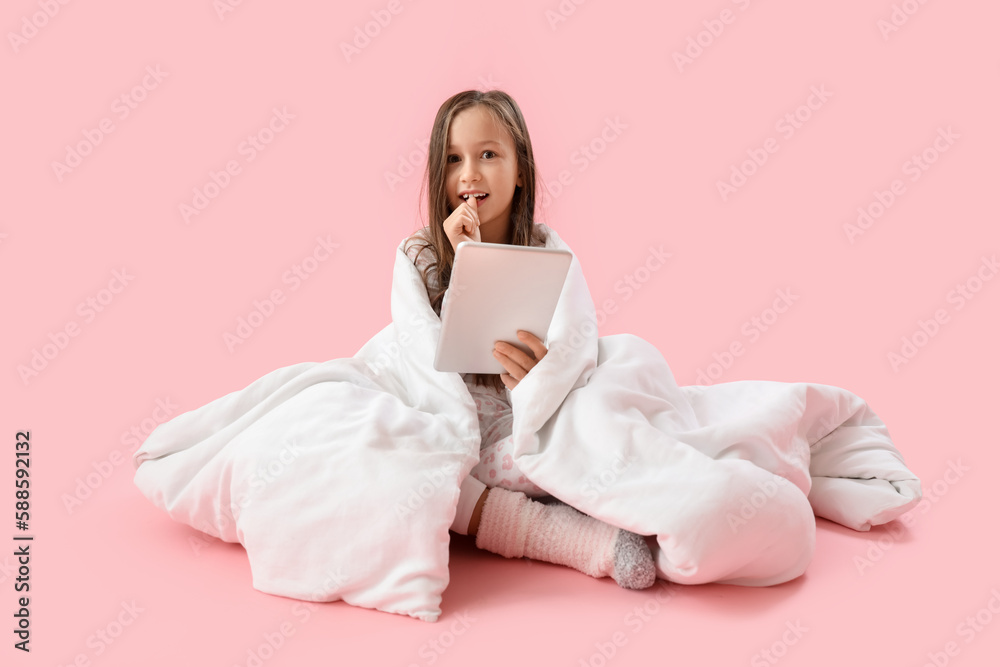 Little girl with blanket and tablet computer biting nails on pink background