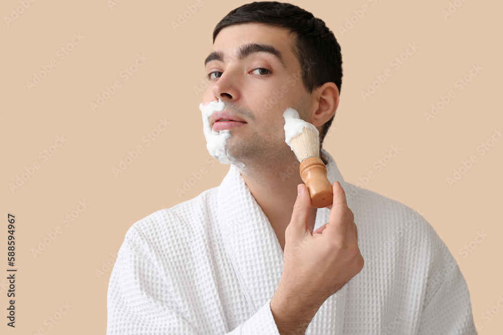 Young man shaving against beige background