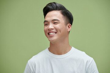 Wall Mural - Portrait shot of young adult Asian man smiling posturing on green wall background