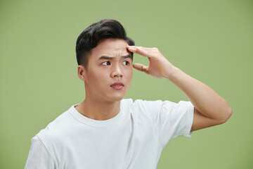 Wall Mural - Anti aging. Handsome young man touching his forehead while standing against green background