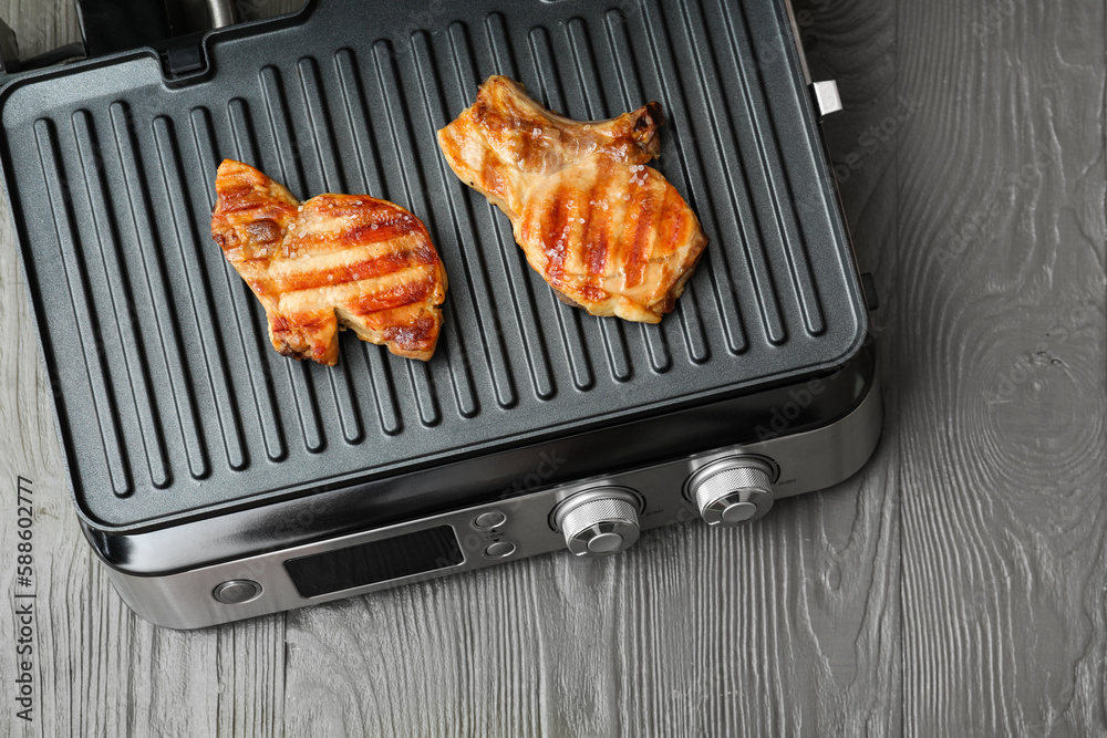 Modern electric grill with delicious steaks on grey wooden table