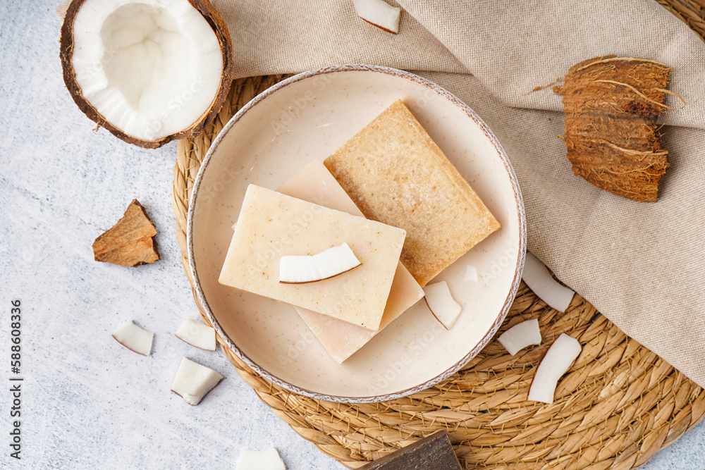 Composition with plate of natural soap bars and coconut on light background