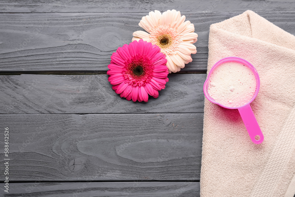 Laundry detergent, gerbera flowers and towel on grey wooden background