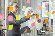 © SOMKID - Asian woman team working on project plan using sticky papers notes on glass wall, people meeting to share idea, Business design planning concepts.