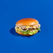 Tasty cheeseburger with onion, cheddar cheese, and sauce on a blue background, reflecting a modern, minimalist food photography style. Perfect for meal on-the-go and presented in a square composition