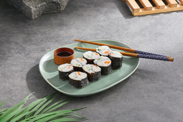 Canvas Print - Modern japanese food concept. Maki sushi on ceramic plate with soy sauce and chopsticks on stone background. Aesthetic composition with sushi roll on dark concrete backdrop. Yin yang maki roll.