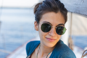 Wall Mural - Happy smiling portrait of a beautiful young girl in sunglasses on a yacht or boat on the coast with the sea in the background.