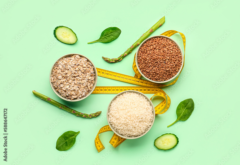 Bowls with different cereals, vegetables and yellow measuring tape on green background. Diet concept
