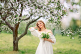 Fototapeta Kwiaty - A beautiful young girl stands among the flowering trees. White flowers. Spring. A girl with her hair in a white dress. Portrait. Romance.