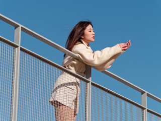 Beautiful young woman with black long hair in white skirt posing eyes closed with blue sky background in sunny day. Emotions, people, beauty, travel and lifestyle concept.