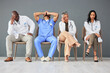 © M Bam/peopleimages.com - Exhausted, tired and doctors waiting in the hospital with frustration, sad and burnout. Upset, professional and team of healthcare workers sitting in a line in a hallway for meeting in medical clinic