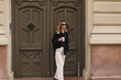 © zvkate - Happy beautiful stylish woman having good fashion white jeans pants, black shirt walking by street, make step and holding coffee or tea in cup takeaway, good mood. Girl look happy, go away from house.