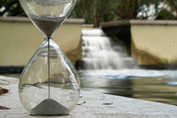 Closeup of an hourglass with flowing sand and a waterfall in the background