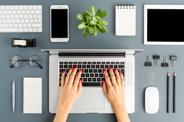 Wall Mural - Female hands working on modern laptop on gray background with accessories. Office desktop. Flat lay