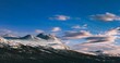 Panoramic shot of a mountain partially in snow under the blue sky and clouds