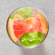 Refreshing grapefruit drink with mint leaves and ice on gray stone table