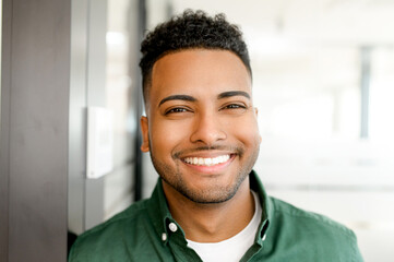 Close-up headshot portrait of successful masculine indian businessman in casual shirt indoors, smiling positive proud male entrepreneur, ceo, manager lookinf at the camera