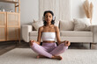 © piksik - Front view on Young fit healthy African American woman in sportswear sitting at home doing yoga, meditating and breathing in the morning. Mental health and wellbeing banner with place for text