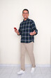 © KrishnaTedjo - Full length photo of Asian man walking and holding mobile phone with happy expression