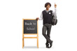 © Ljupco Smokovski - African american student in a uniform leaning on blackboard with text back to school and pointing up